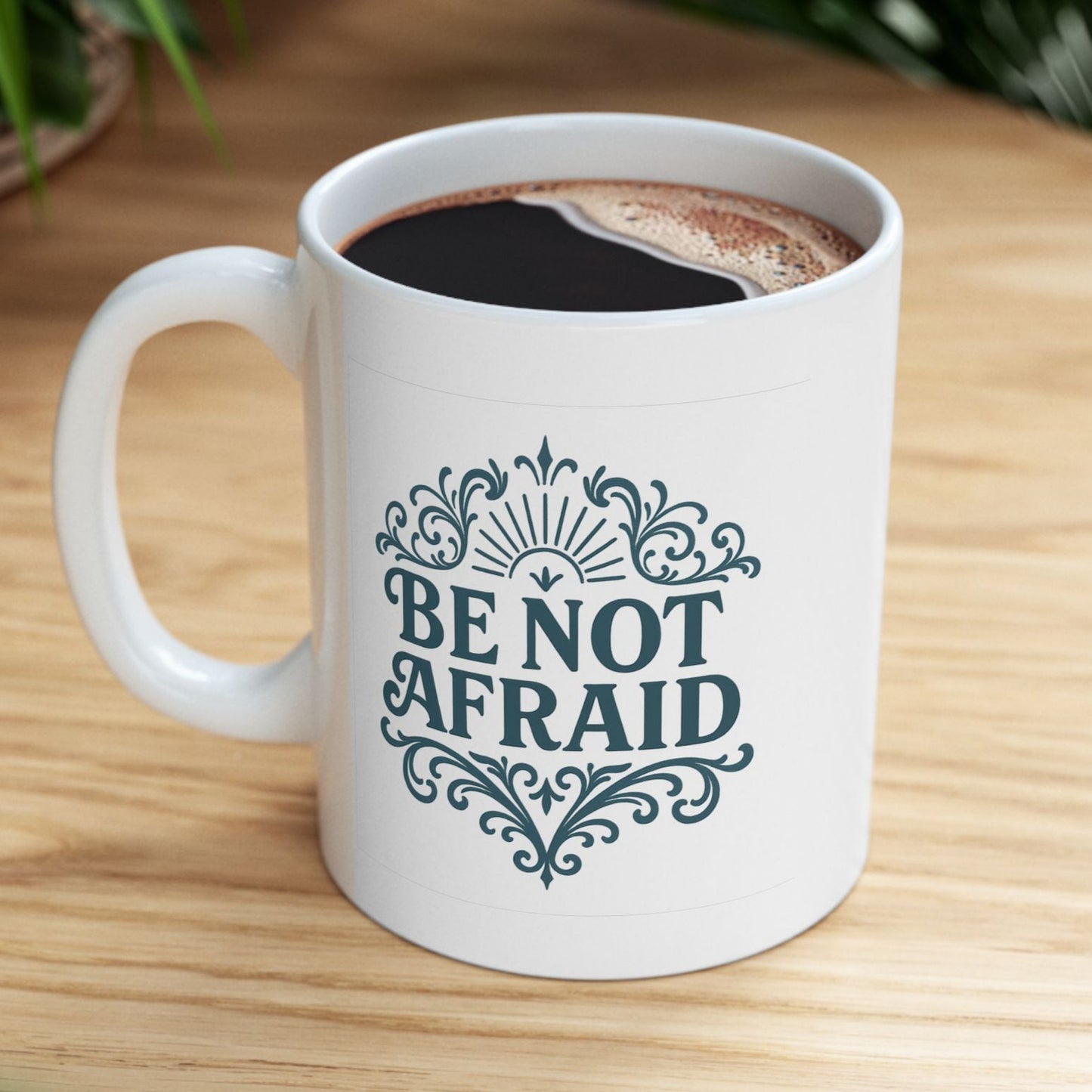 White mug with 'Be Not Afraid' text on a wooden table with coffee.