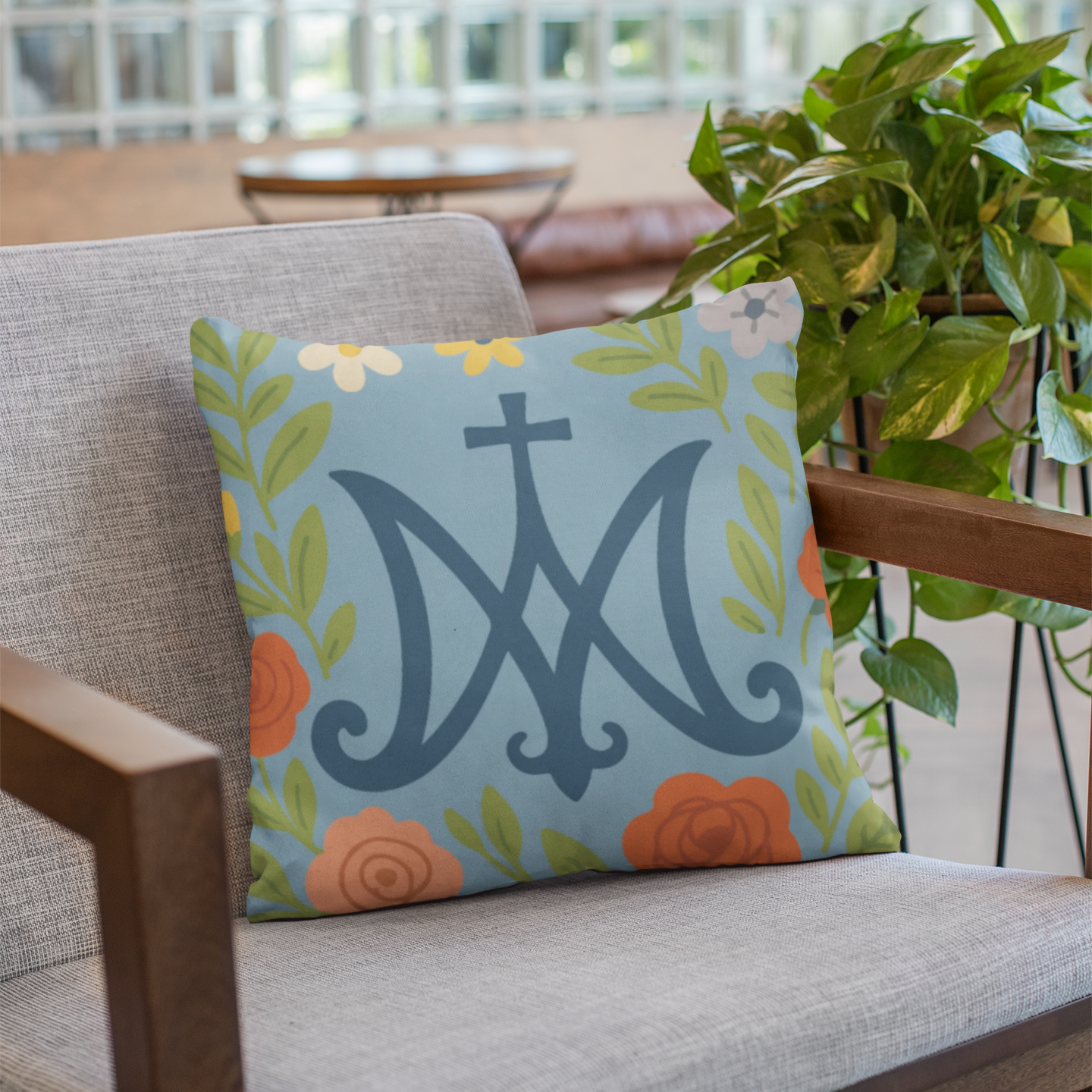 Decorative pillow with floral design and Marian Catholic symbol on a chair indoors.